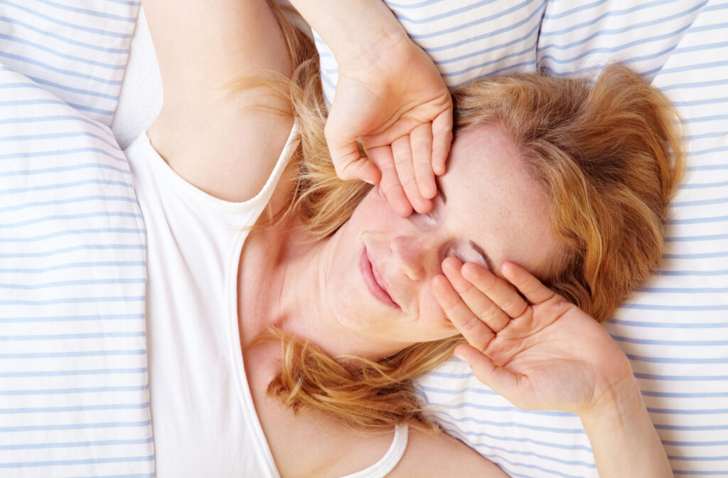 A woman lying in bed rubbing her eyes with her hands.