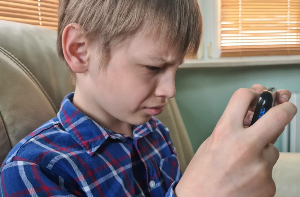 A child sitting on a couch and holding a smartphone very close to his face.
