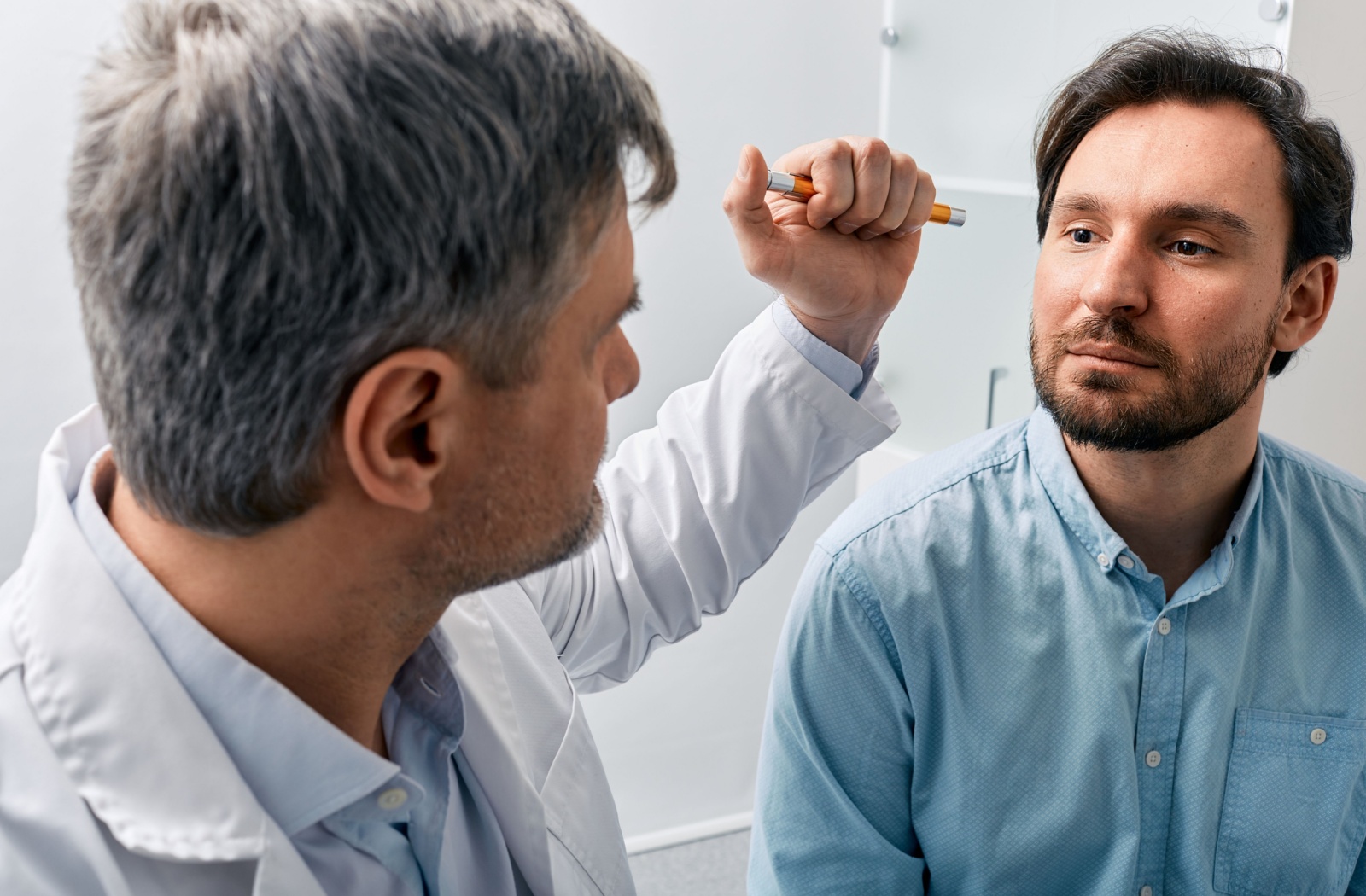 An optometrist examines their patient's pupil reflex during an eye exam.