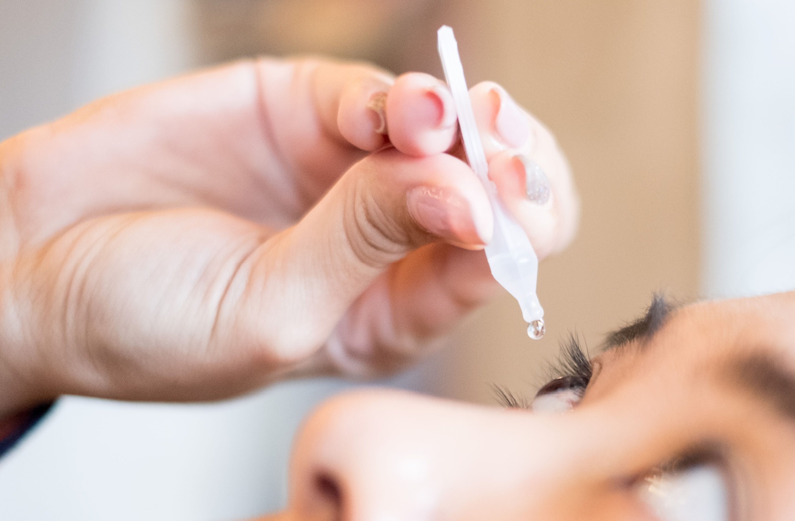 A close up view of a woman putting artificial tears in her right eye.