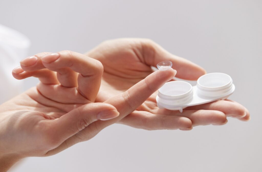 A close-up image of a woman holding a contact lens case in one hand with a contact lens sitting on the tip of an extended finger.