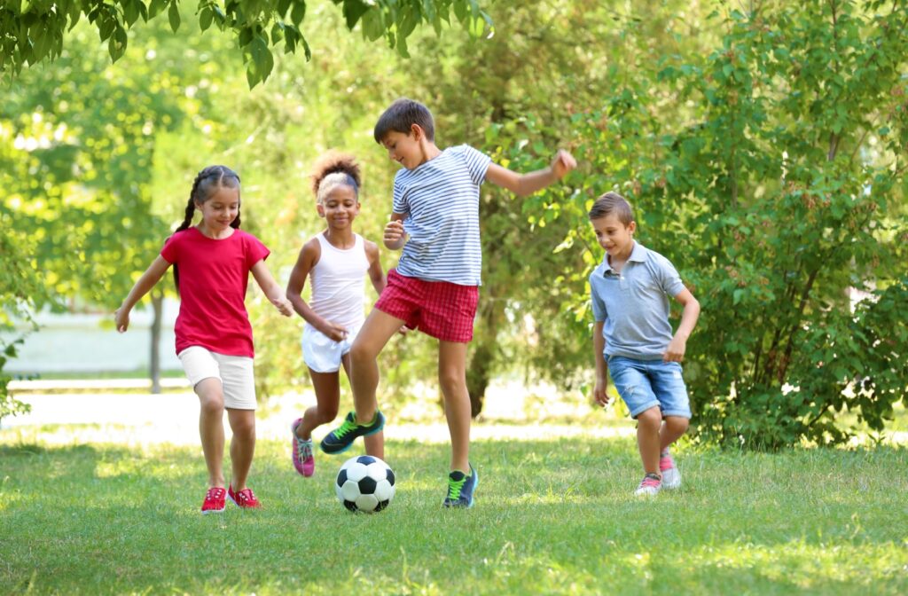 A group of children plays soccer in a grassy park on a sunny day, as sunlight exposure can help with myopia progression.