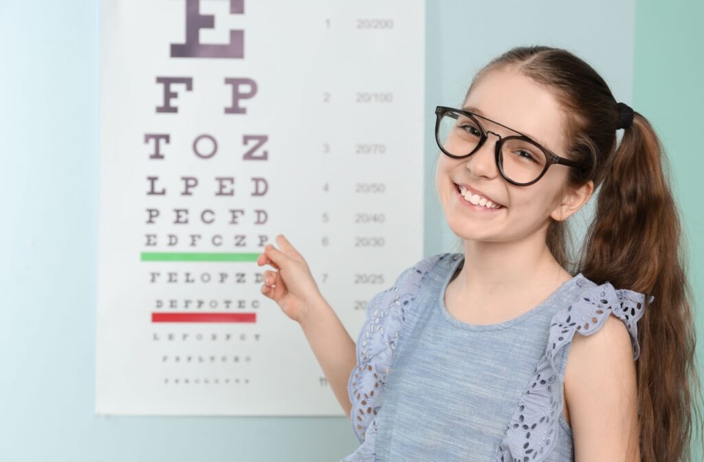 A child wearing a pair of trendy eyeglasses to correct their myopia points at a Snellen eye chart in an optometrist's office.