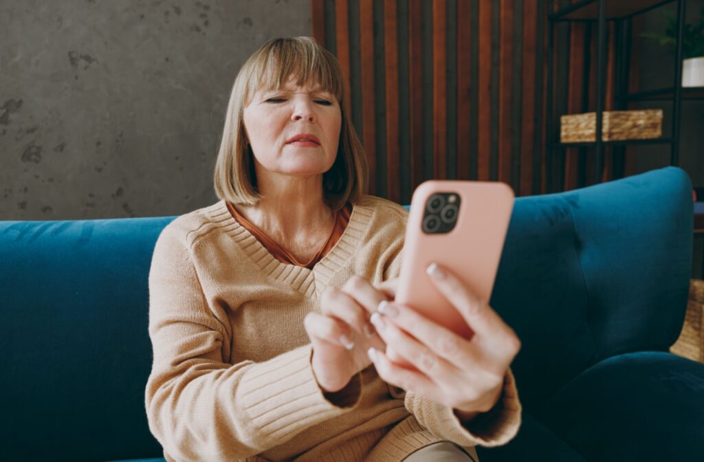 A person holds their smartphone at a distance and squints their eyes to try and see better.