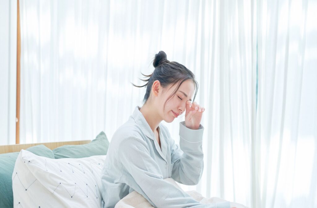 A woman sits up in bed after waking up and rubs her eyes