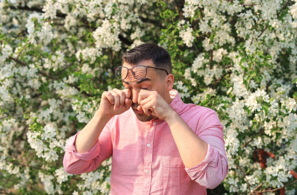 A person standing beside flowers and rubbing their eyes