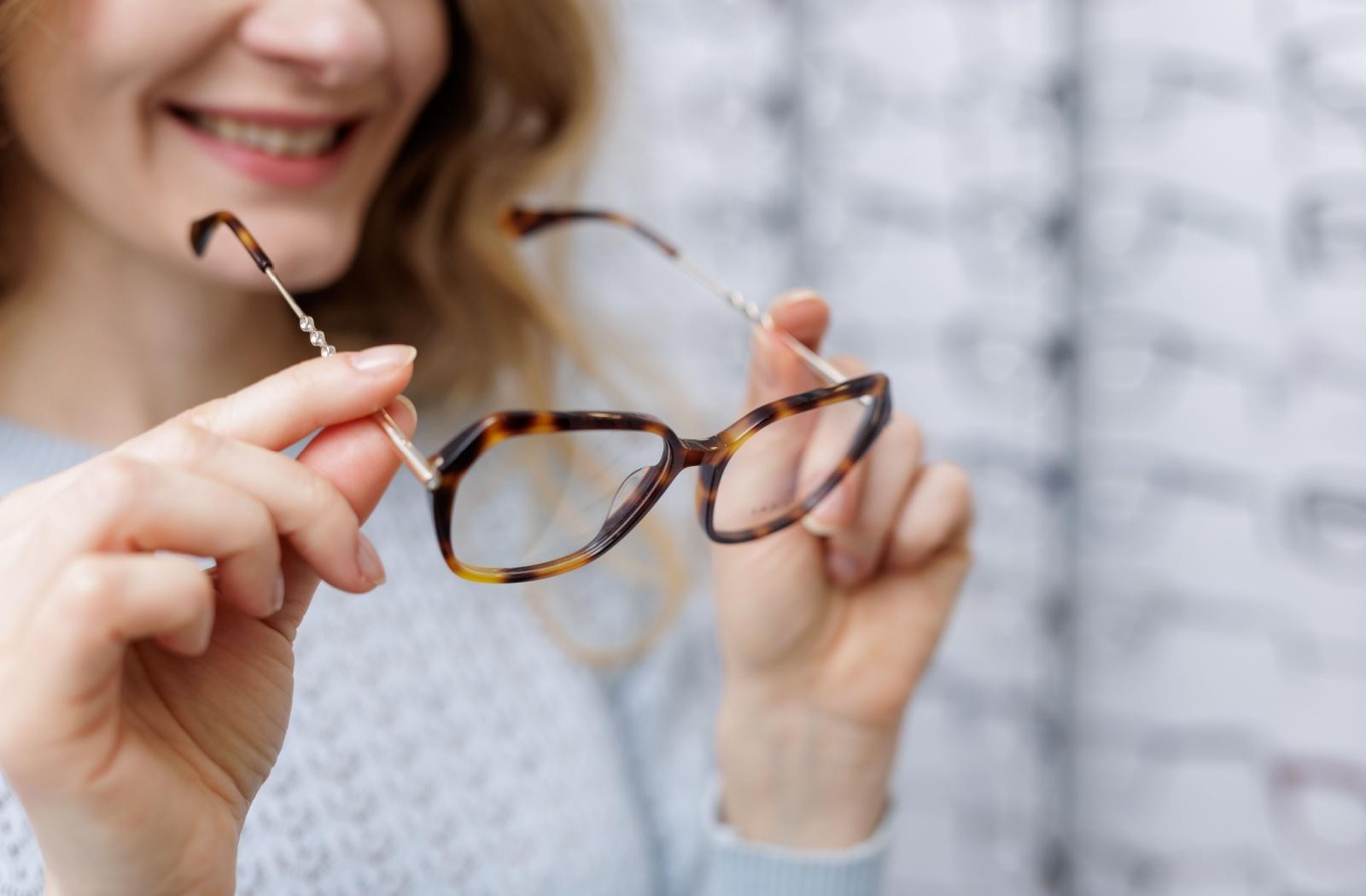 A person holding a pair of glasses at the eye clinic and smiling