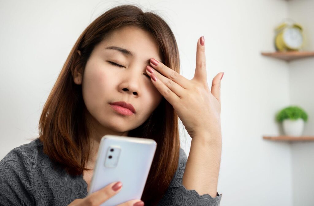 A person using their phone and rubbing their eyes from eye irritation