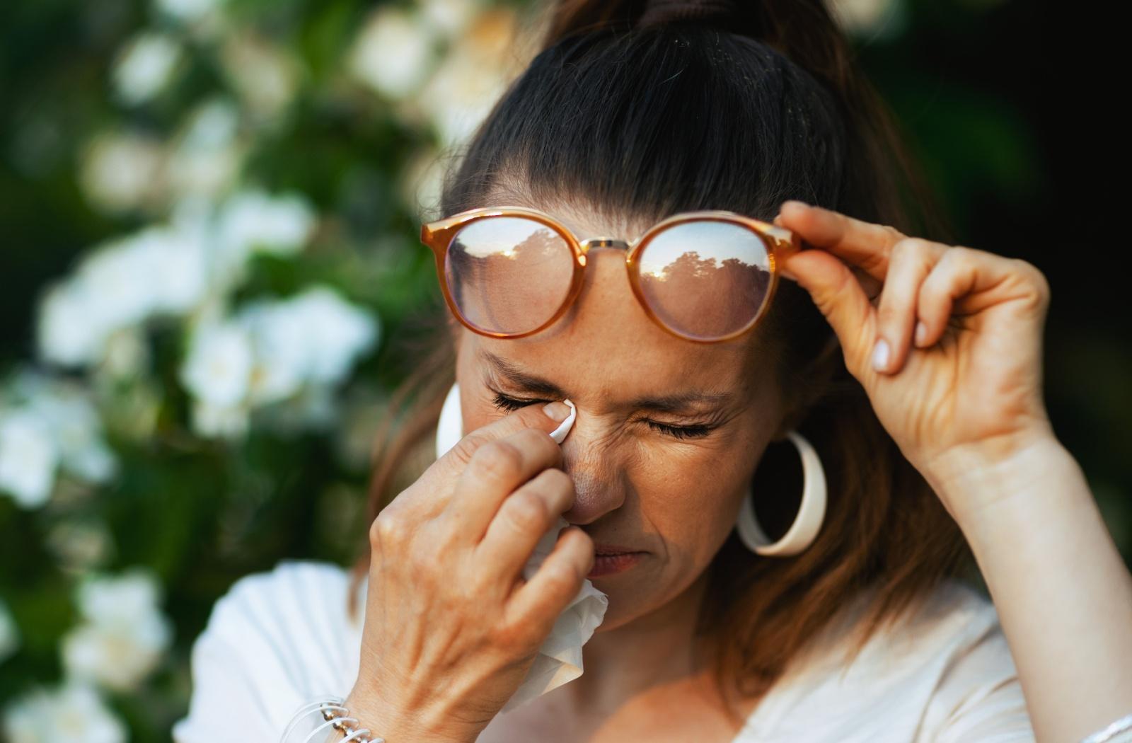 A person dabbing their eye with a tissue due to seasonal allergies