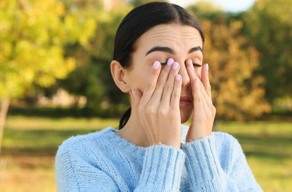A person rubbing their eyes while outside due to seasonal allergies
